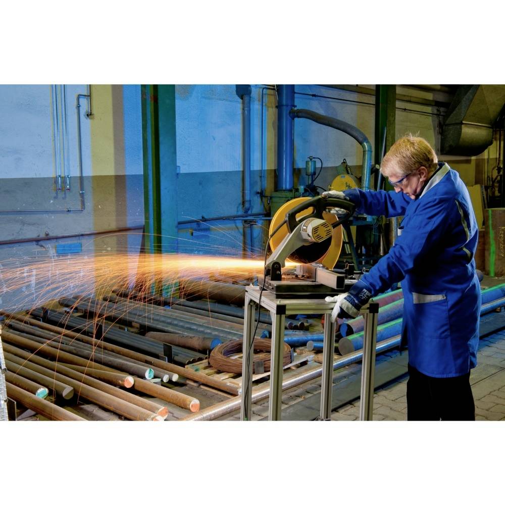 Osoba w odzieży ochronnej używa w warsztacie przecinarki, która wytwarza iskry podczas cięcia rur metalowych.