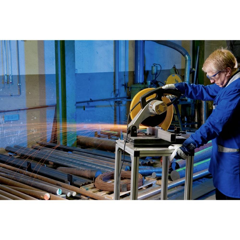 Mężczyzna w okularach ochronnych i rękawicach tnie metalowe rury piłą tarczową w warsztacie. Podczas pracy lecą iskry.