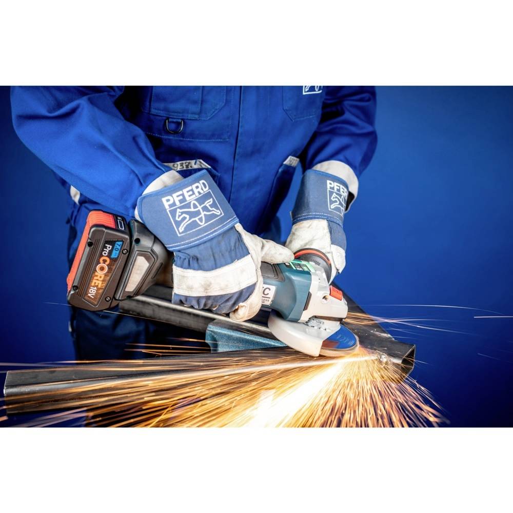 Robotnik w niebieskim stroju ochronnym szlifuje metalową rurę kątrówką, z której tryskają pomarańczowe iskry.