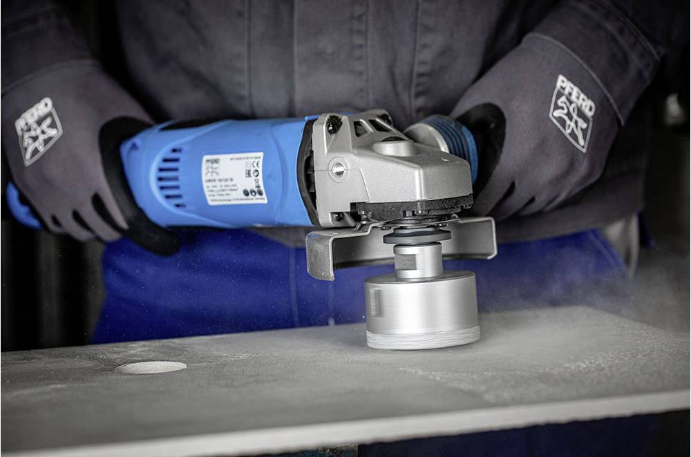 Osoba używa szlifierki kątowej na metalowej powierzchni, a iskry się sypią. Ubranie ochronne nosi logo firmy.