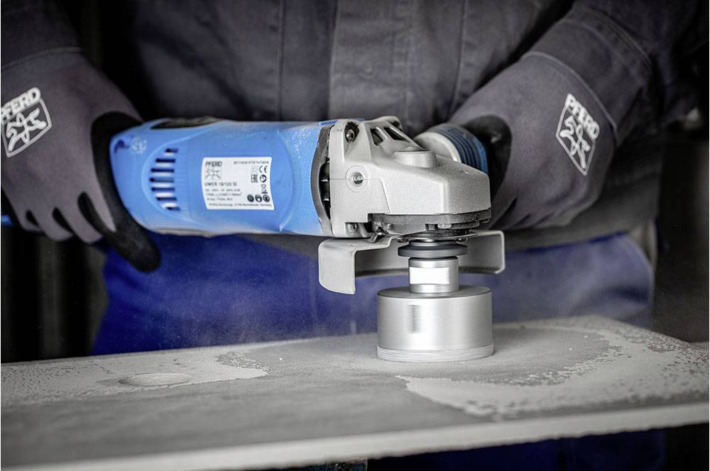 Osoba szlifuje metal niebieską elektryczną szlifierką kątową. Podczas obróbki materiału powstaje pył.