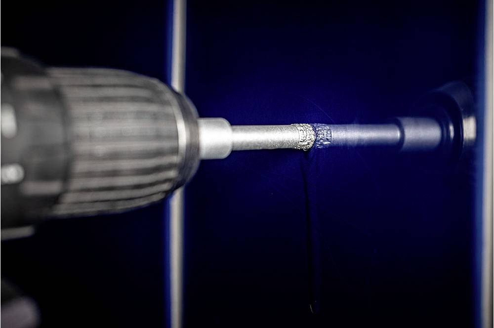 Akumulatorowa wiertarka wywierca małą dziurkę w ciemnoniebieskiej ścianie, przy czym spada trochę pyłu.