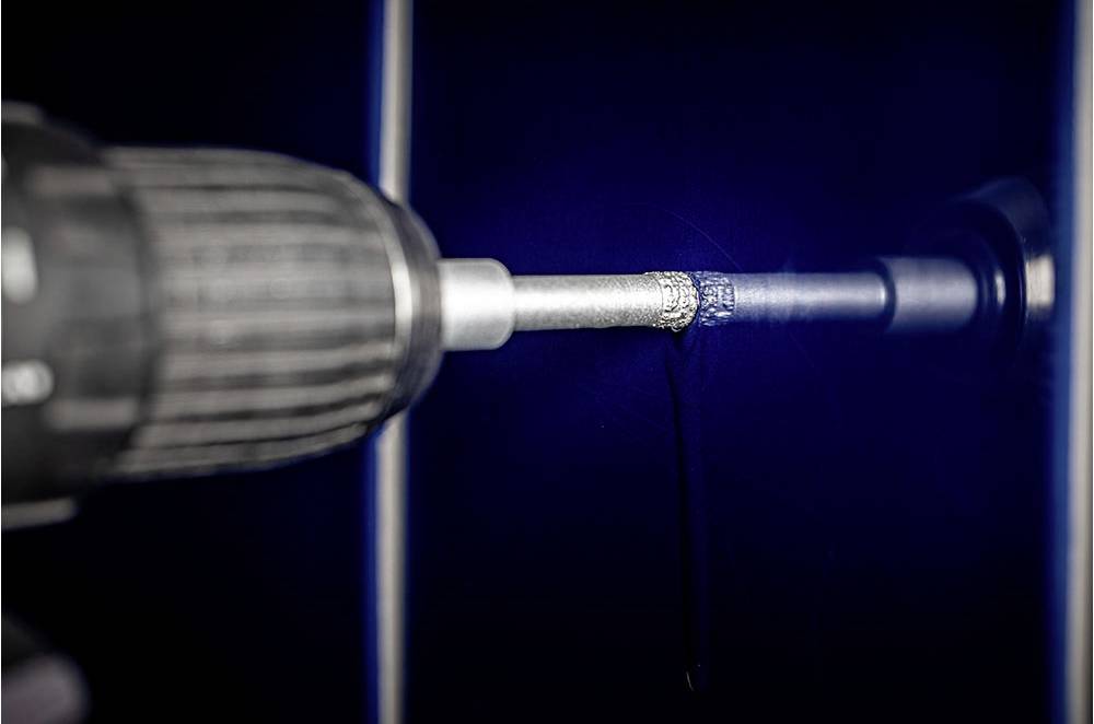 Wiertarka wierci otwór w niebieskiej ścianie. Wiertło obraca się, wchodząc w gładką powierzchnię.