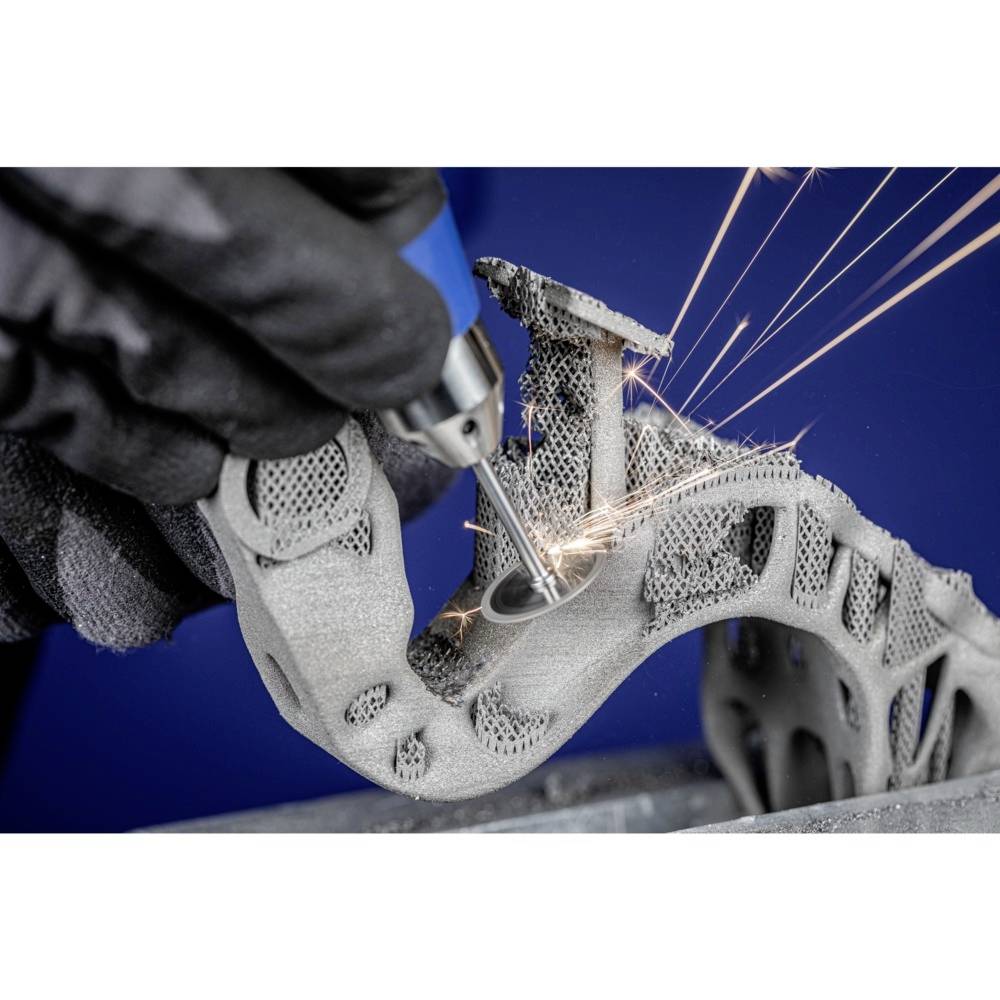 Osoba obrabia złożoną, metalową część wydrukowaną w technologii 3D przy pomocy narzędzia, podczas gdy iskry się sypią.