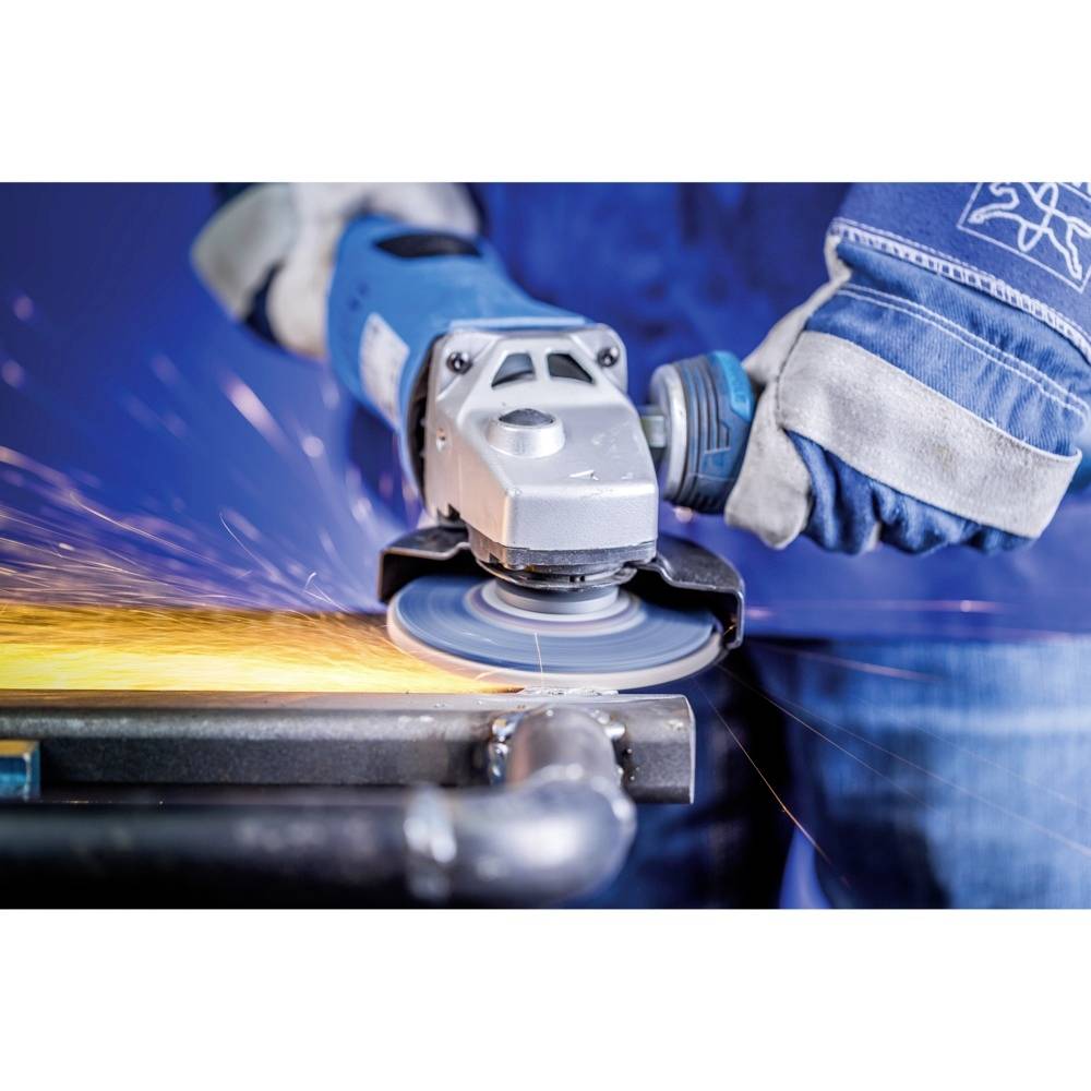 Robotnik w niebieskim ubraniu ochronnym szlifuje metal szlifierką kątową. Od punktu szlifowania odlatują iskry.