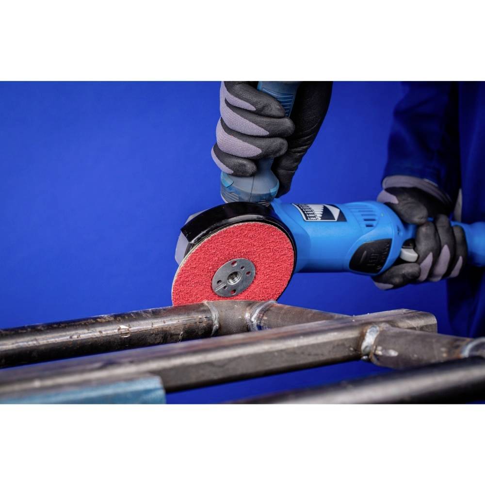 Osoba szlifuje metal niebieską szlifierką kątową, której tarcza jest czerwona. Nosi rękawice ochronne.