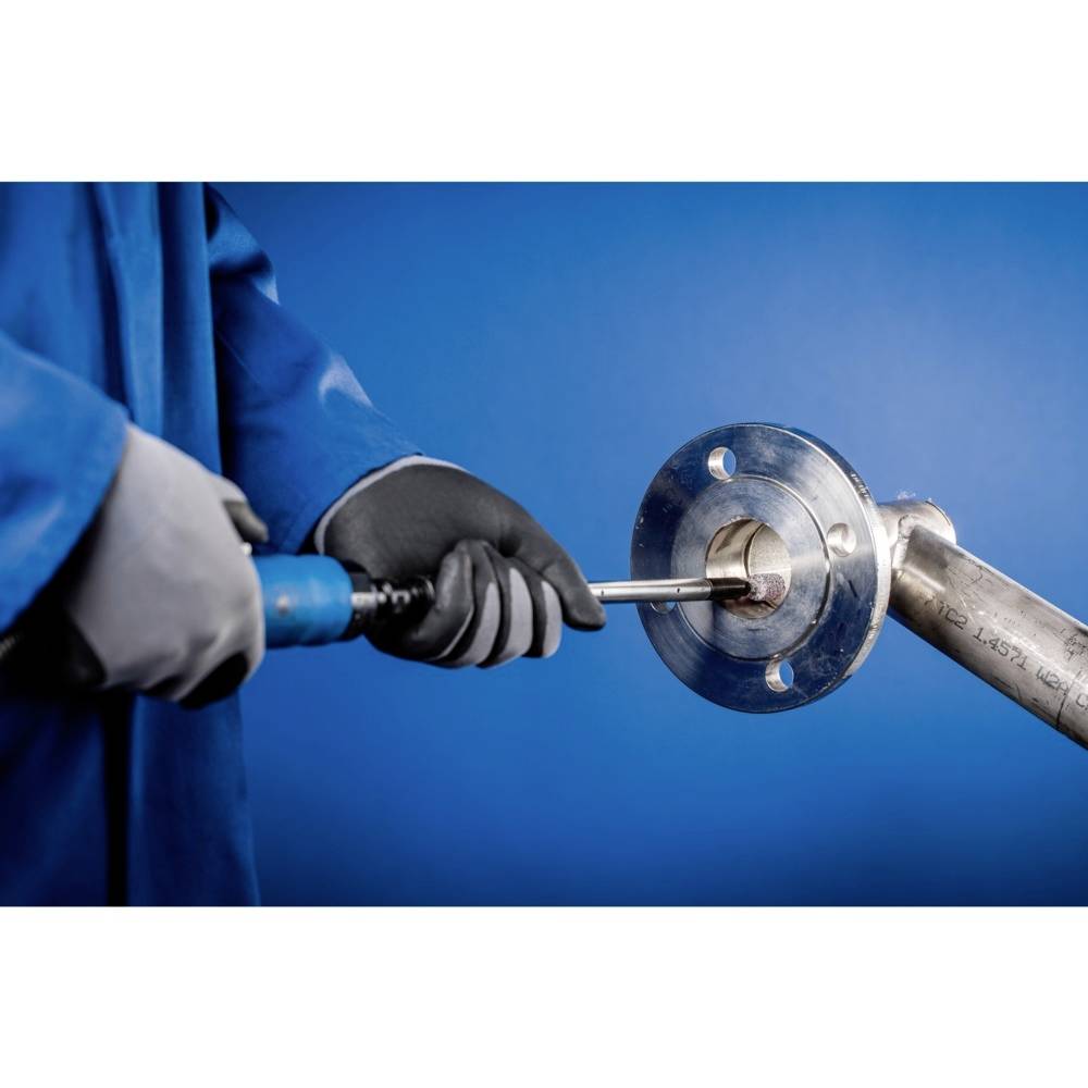 Technik w niebieskim ubraniu roboczym trzyma narzędzie do obróbki metalowego złącza kołnierzowego w środowisku przemysłowym.