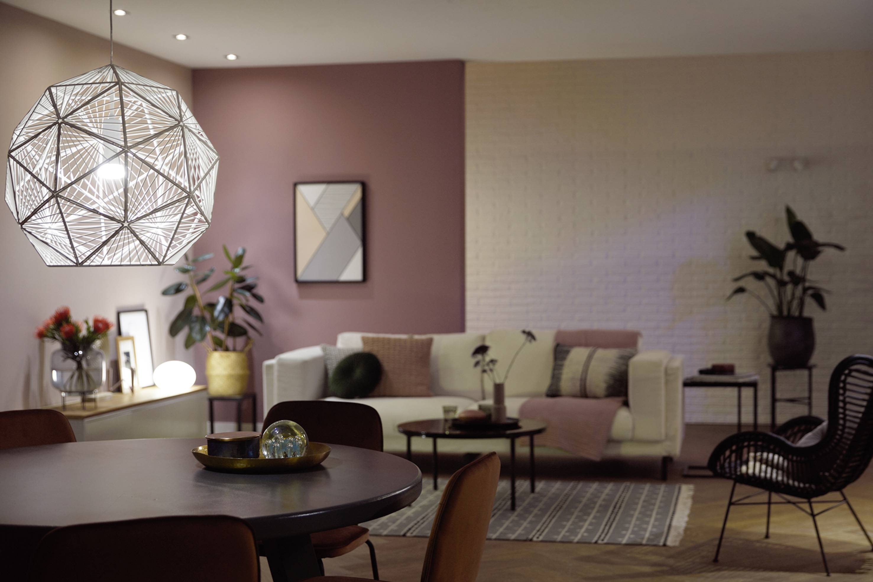 Przytulny salon z nowoczesnym oświetleniem. Biała sofa, rośliny i dzieła sztuki tworzą relaksującą atmosferę.