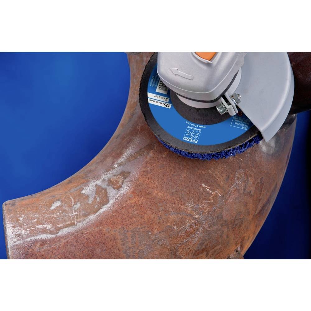 Szlifierka kątowa szlifuje zardzewiałą stal. Tarcza szlifierska jest niebieska, a tło jest jednolicie niebieskie.