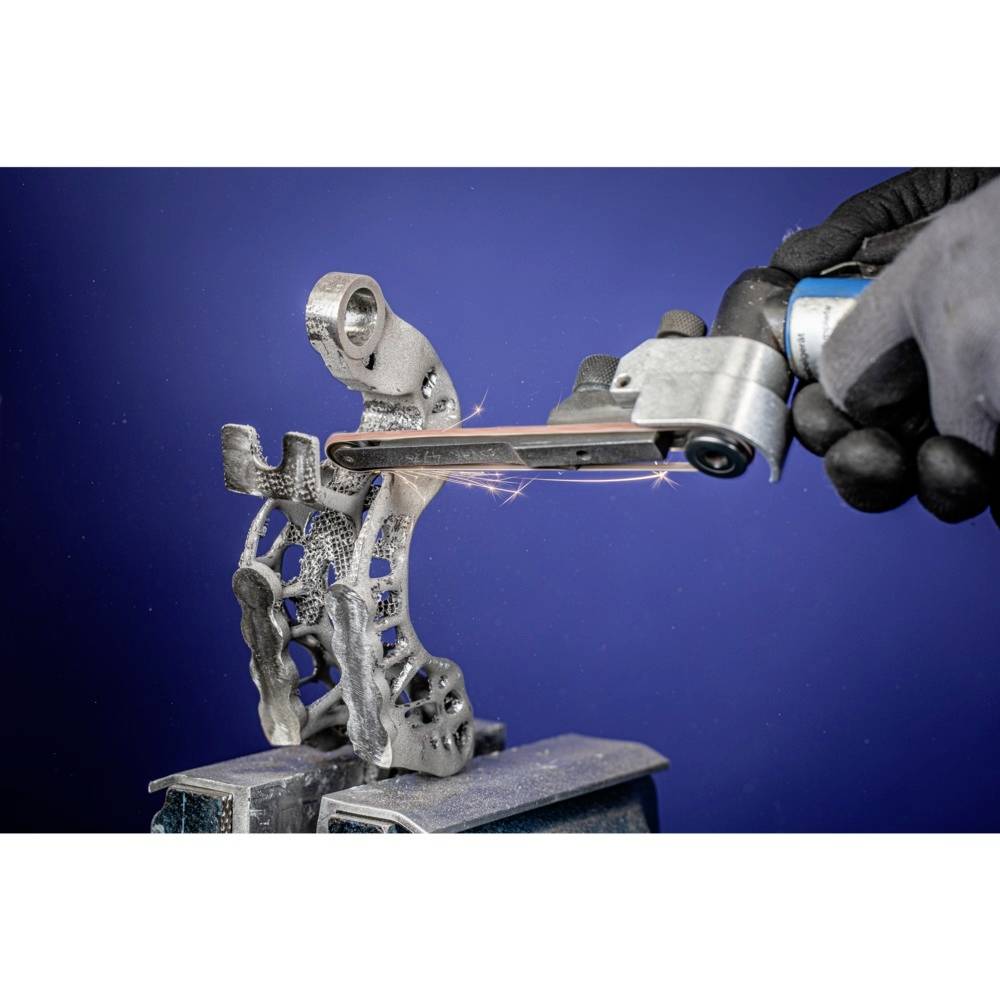 Osoba obrabia metalowy element za pomocą narzędzia szlifierskiego. Element ma skomplikowany, delikatny wzór.