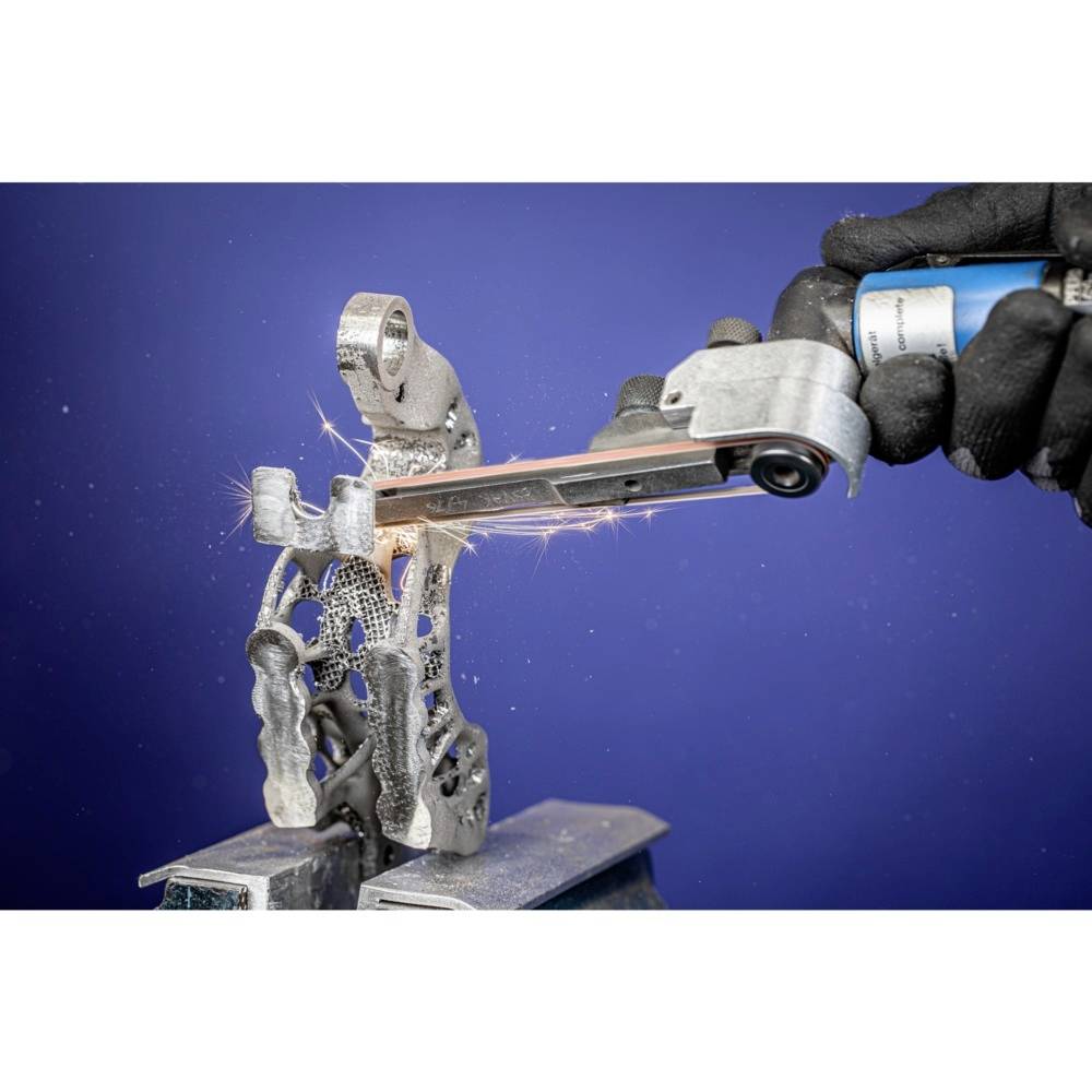 Osoba obrabia złożoną, metalową strukturę wydrukowaną w technologii 3D za pomocą urządzenia szlifierskiego, iskry się sypią.