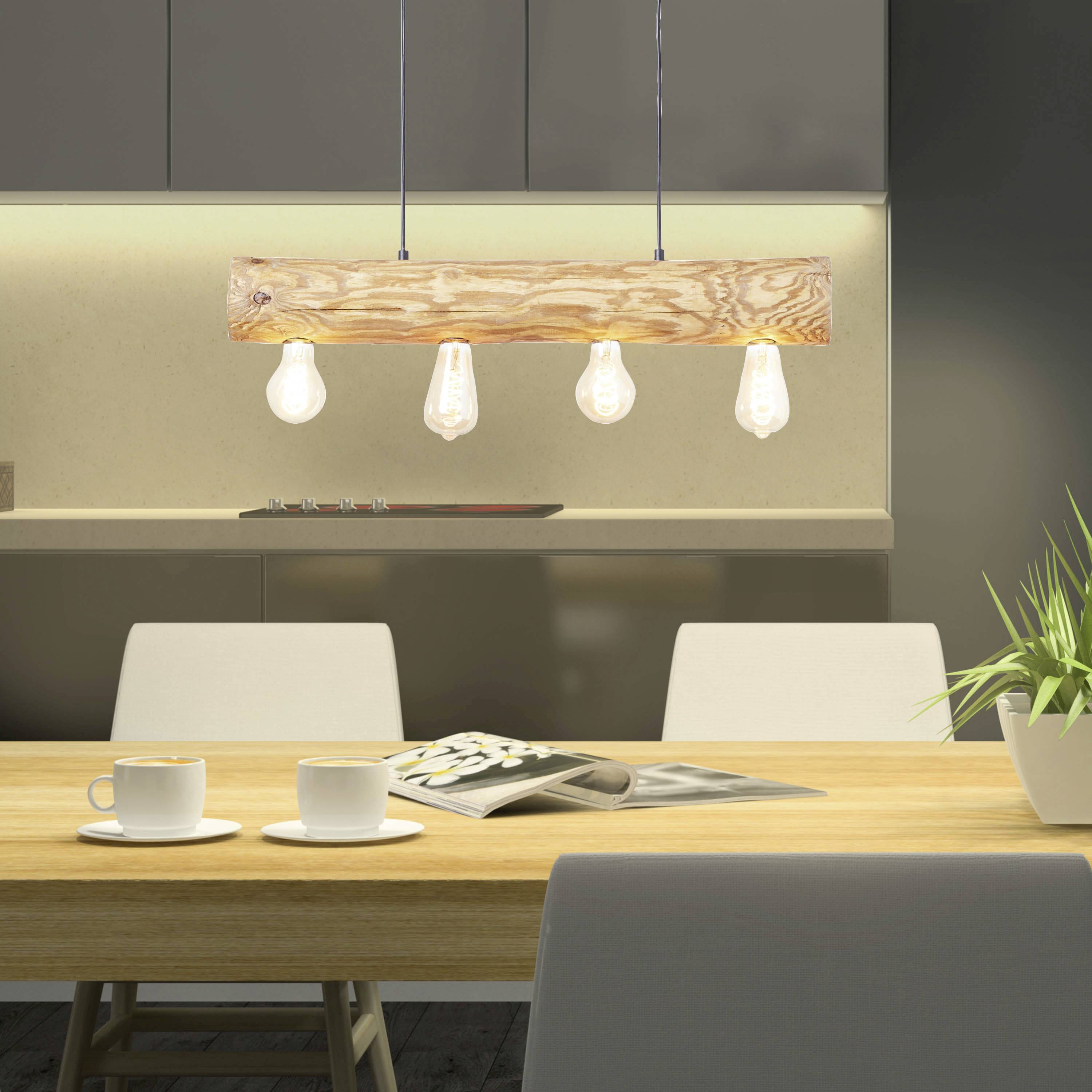 Nowoczesna kuchnia z drewnianą lampą wiszącą nad stołem jadalnianym, na którym leżą białe filiżanki i magazyn. Ciemne szafki w tle.