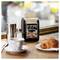 Na stole stoją kubek, croissant i dozownik papieru z napisem 'Let us cater your next breakfast meeting'.