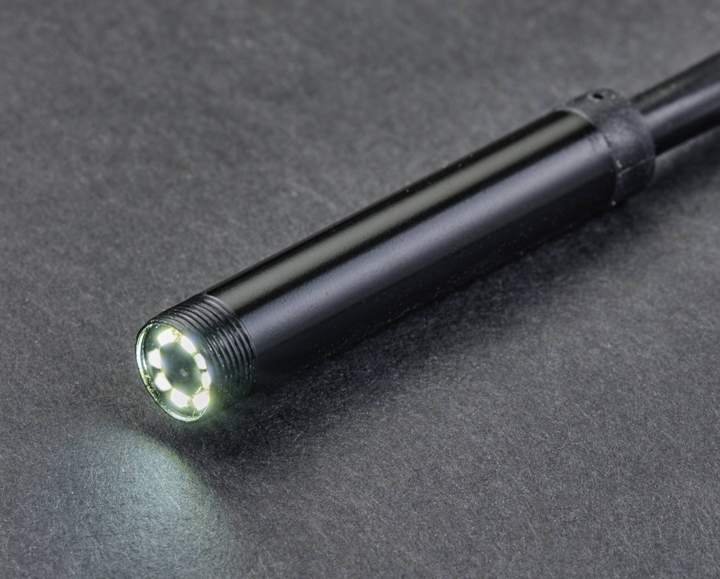 Zbliżenie czarnego endoskopu z podświetlaną kamerą. Leży na szarej powierzchni.