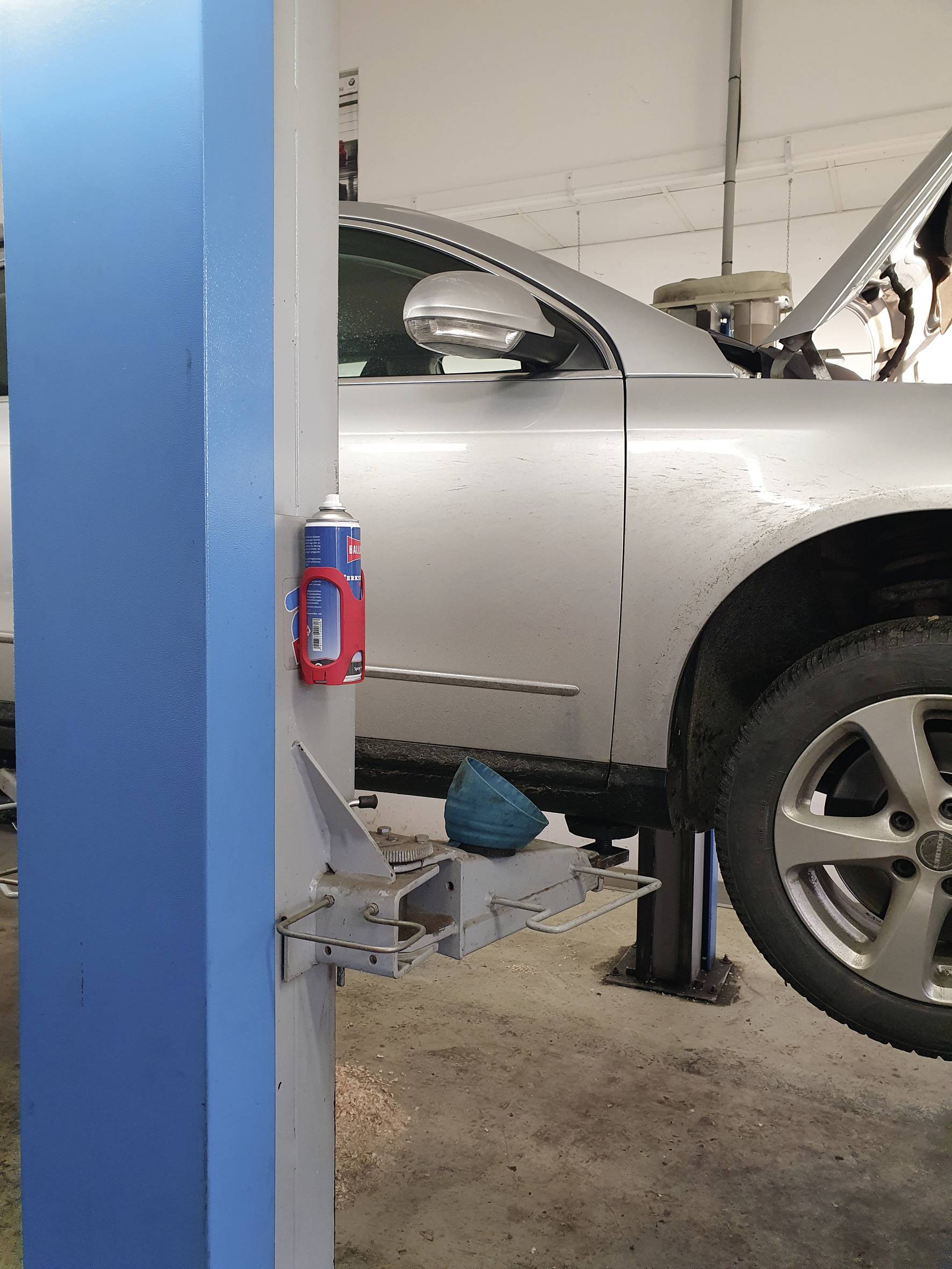 Srebrny samochód jest podniesiony na podnośniku w warsztacie. Maska jest otwarta, a narzędzia są widoczne.