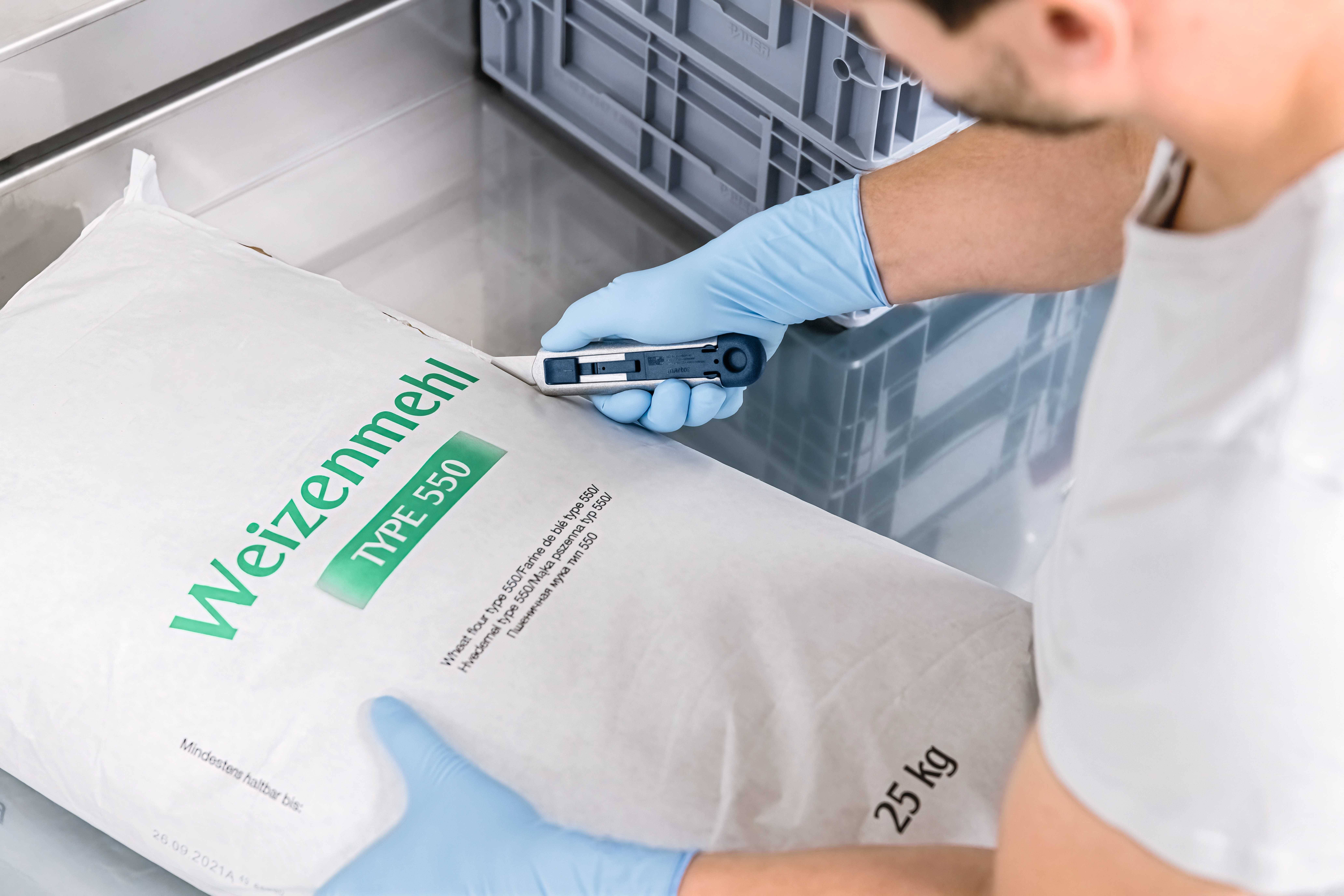 Osoba skanuje za pomocą czytnika kodów kreskowych 25-kilogramowy worek mąki pszennej typ 550.