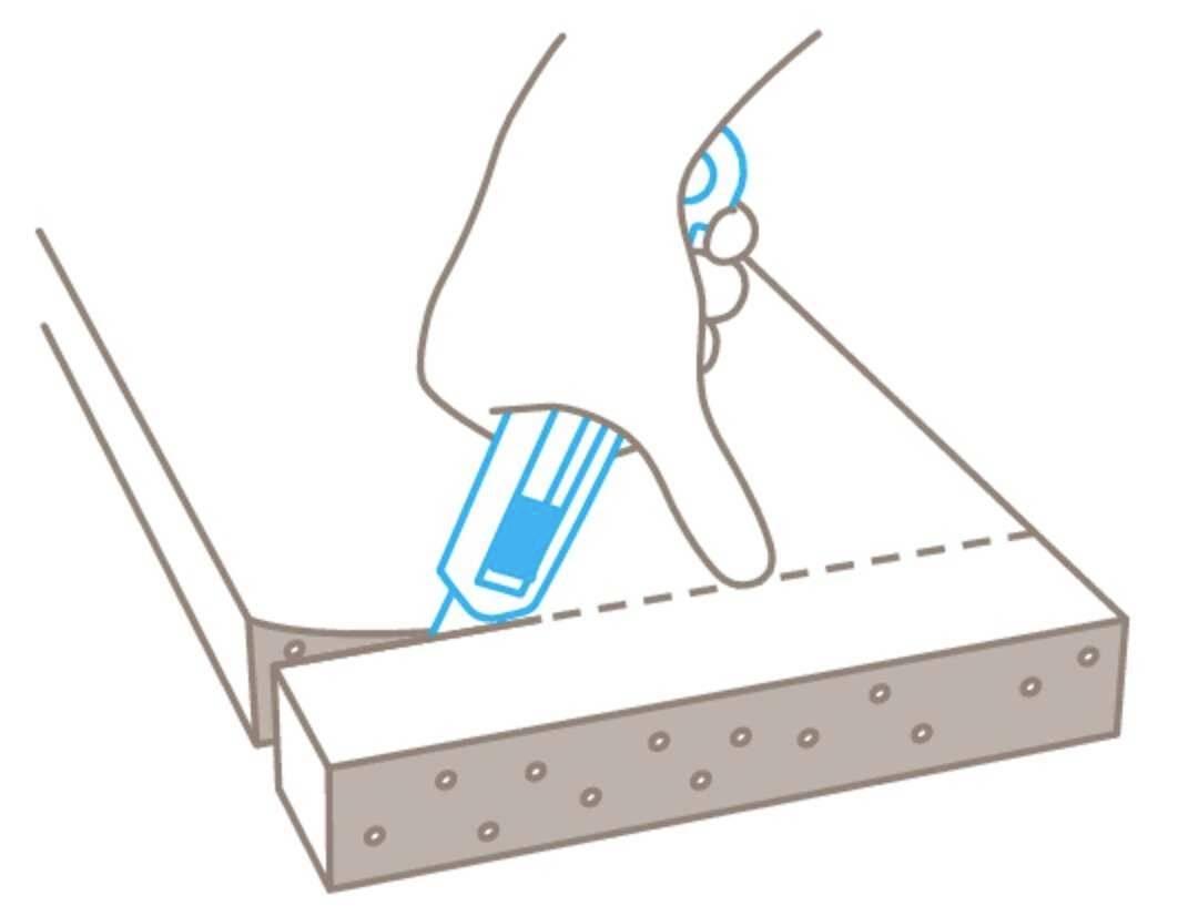 Jedna ręka trzyma niebieski nóż introligatorski i wycina wzdłuż linii przerywanej przez kawałek materiału.