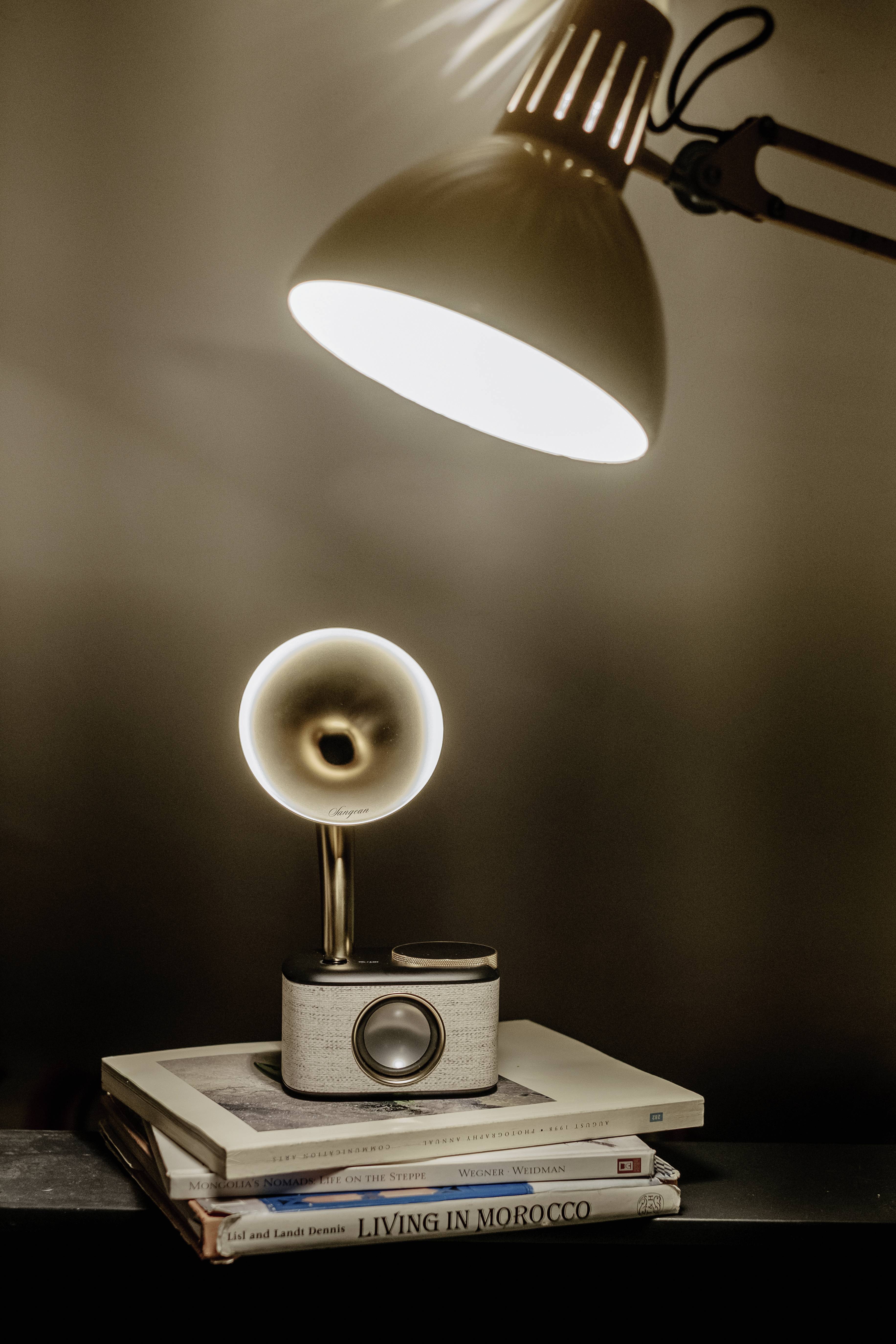 Stylowa, minimalistyczna lampka nocna oświetla stos książek leżących na stole. Lampa rzuca ciepłe, przytulne światło.