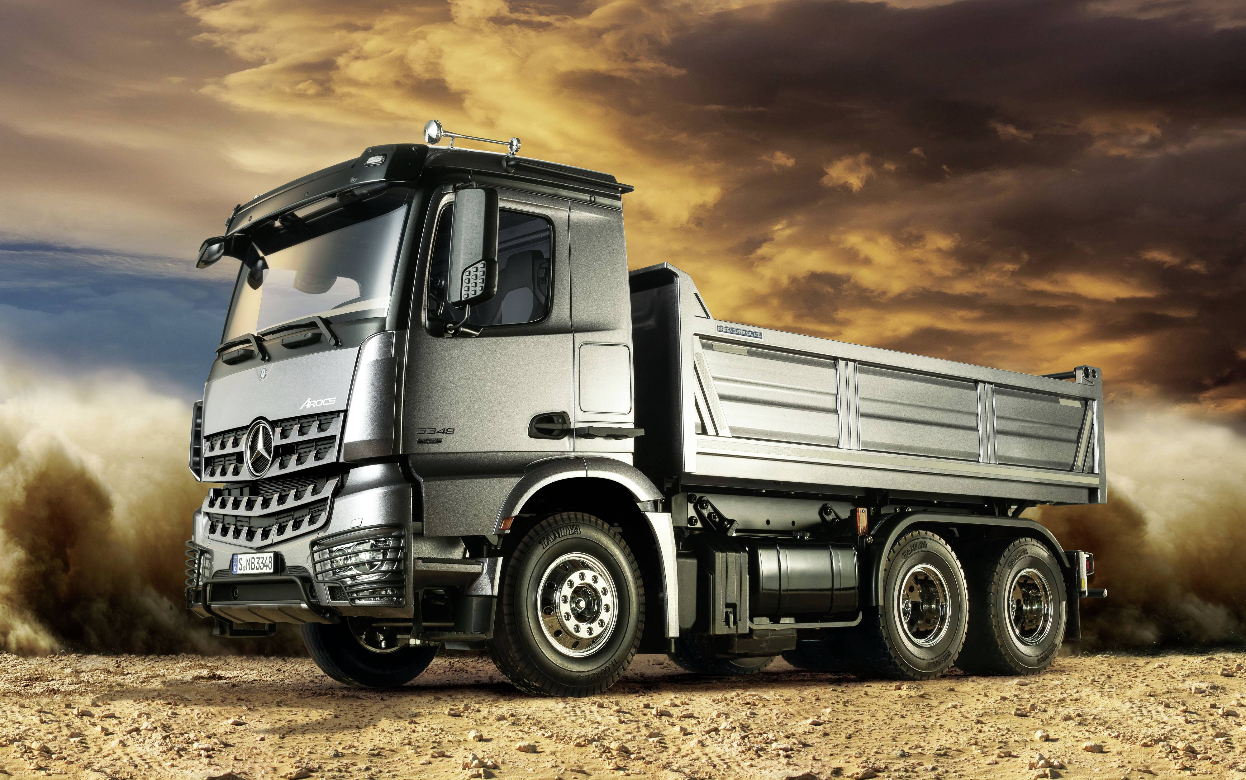 Ciężarówka stoi na pylistej drodze na tle dramatycznie zachmurzonego nieba. Pojazd jest przygotowany do załadunku.