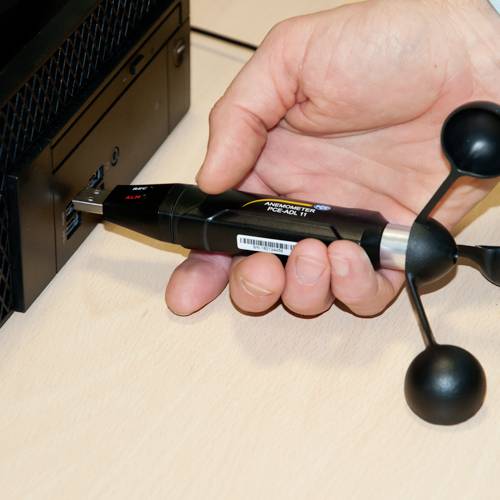 Jedna ręka trzyma przyrząd pomiarowy z dwoma czarnymi kulami, podłączony do komputera. Prawdopodobnie mierzy on promieniowanie.