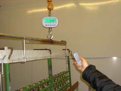 Osoba trzyma pilota, podczas gdy duży przedmiot wisi na elektronicznej wadze zawieszeniowej z wyświetlaczem.