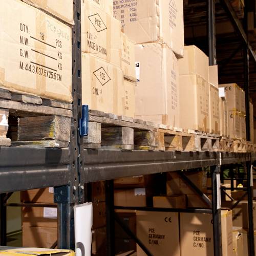 Kartony ułożone na metalowych regałach w magazynie. Niektóre kartony są oznaczone etykietą "Made in China".