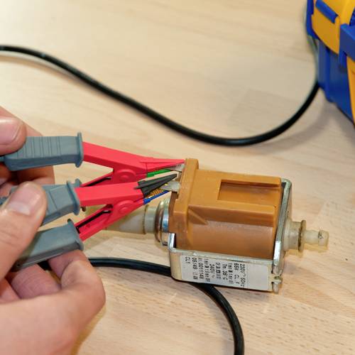 Osoba testuje silnik elektryczny za pomocą dwóch czerwonych zacisków krokodylkowych. Dłonie regulują zaciski do celów pomiarowych.