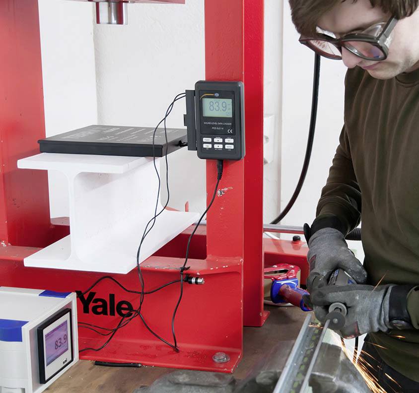 Mężczyzna w okularach ochronnych tnie metal z wiązką iskier. W tle stoi czerwona maszyna z cyfrowymi wyświetlaczami.