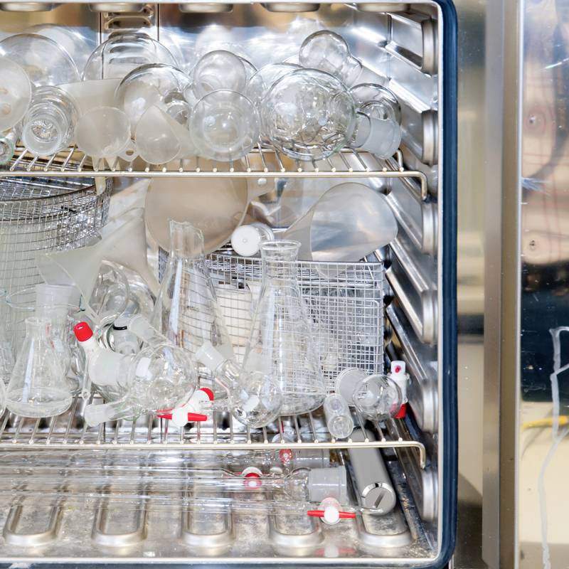 Zmywarka laboratoryjna jest wypełniona kolbami, kolbami Erlenmeyera i probówkami ułożonymi w stosie do czyszczenia.