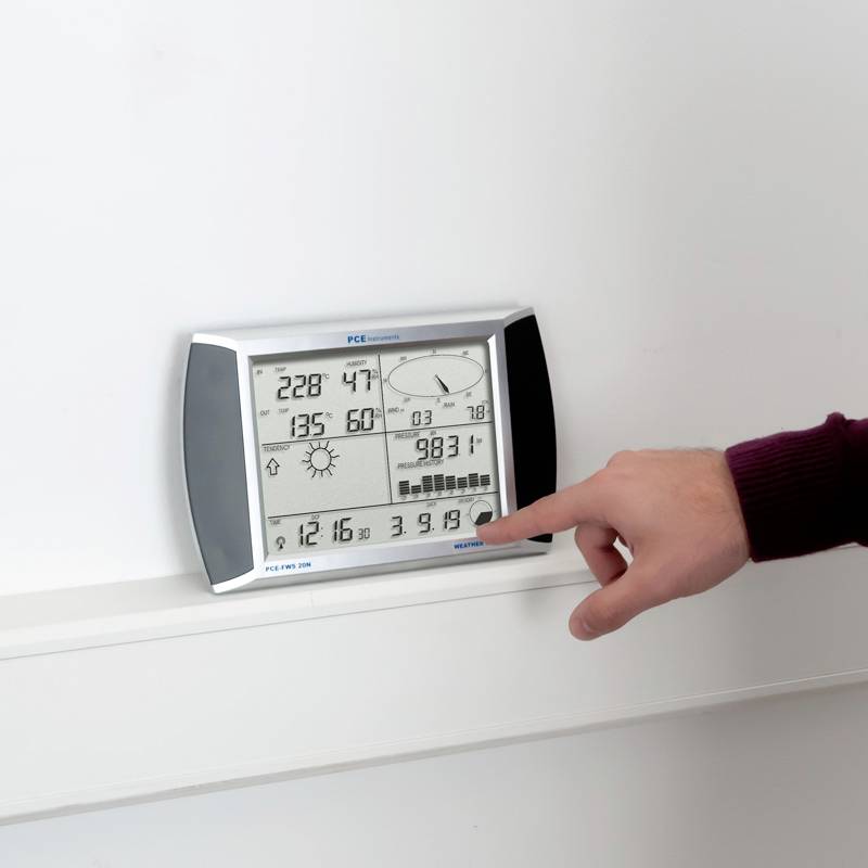 Osoba wskazuje na elektroniczny przyrząd pomiarowy z wyświetlaczem cyfrowym. Widoczne są dane dotyczące temperatury, wilgotności i ciśnienia.