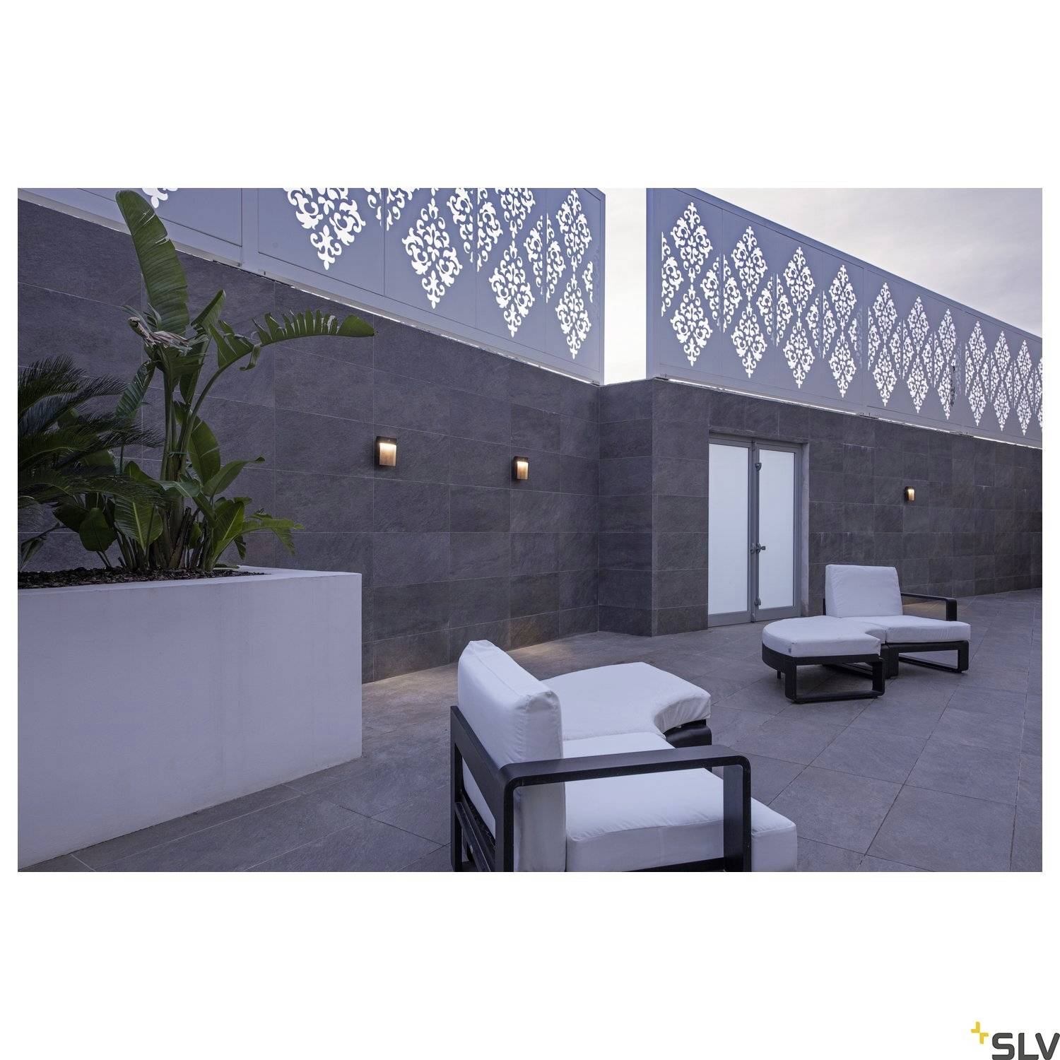 Taras dachowy z nowoczesnymi meblami i roślinami. Białe ozdoby zdobią szarą ścianę. Strefa relaksu z dwoma fotelami.