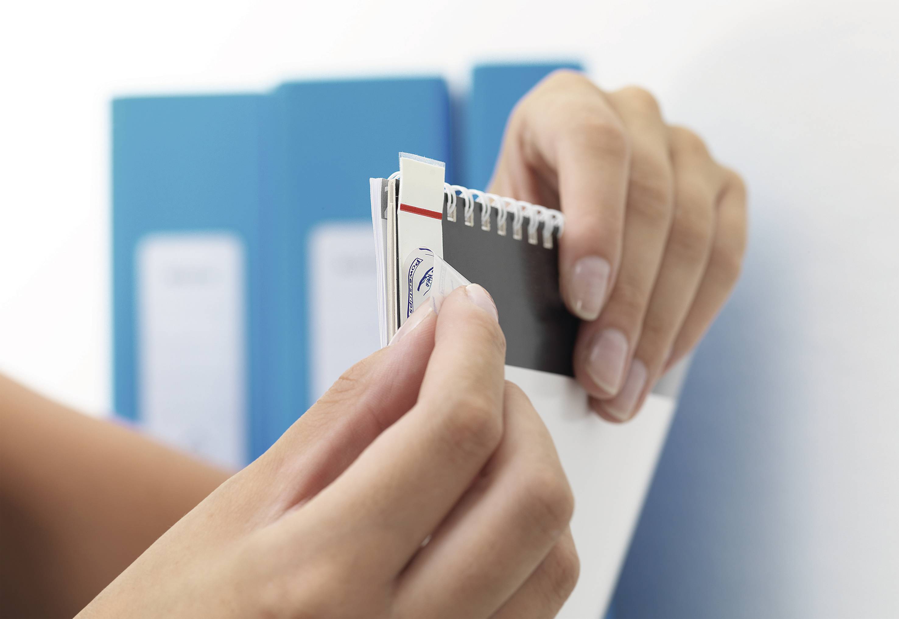 Osoba przegląda próbnik kolorów przed niebieskimi segregatorami. Wyciąga jeden wzór koloru.