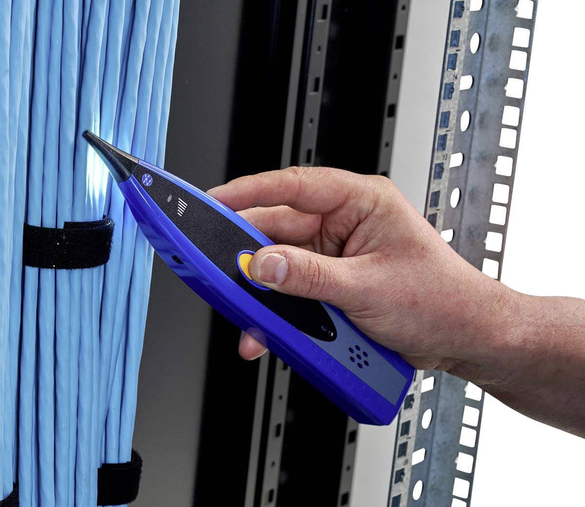 Jedna ręka trzyma niebieskie urządzenie pomiarowe przy wiązce niebieskich kabli, prawdopodobnie w serwerowni lub szafie telekomunikacyjnej.