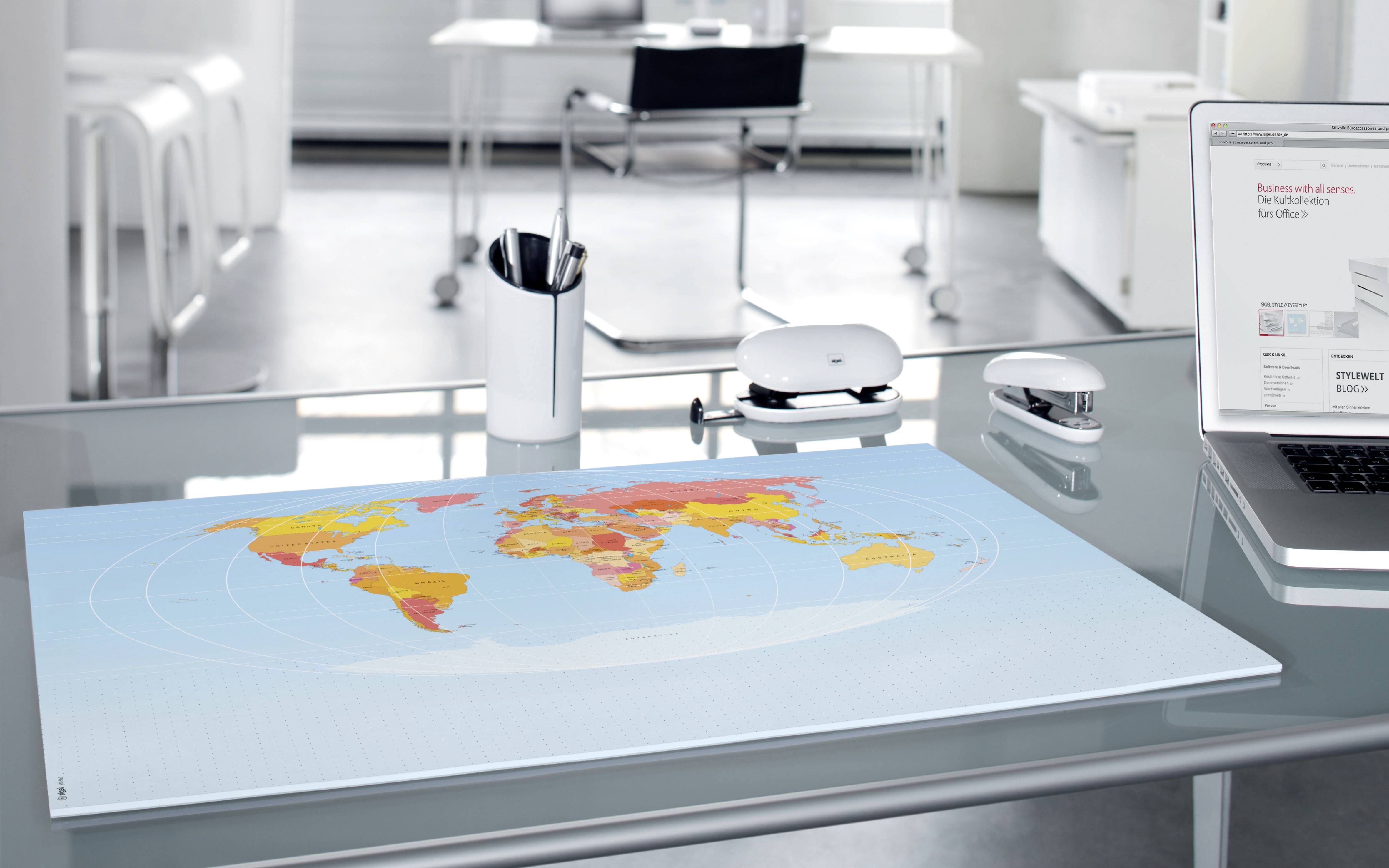 Biuro z nowoczesnym biurkiem, na którym leży mapa świata. Otwarty laptop z widoczną stroną internetową; w tle meble biurowe.