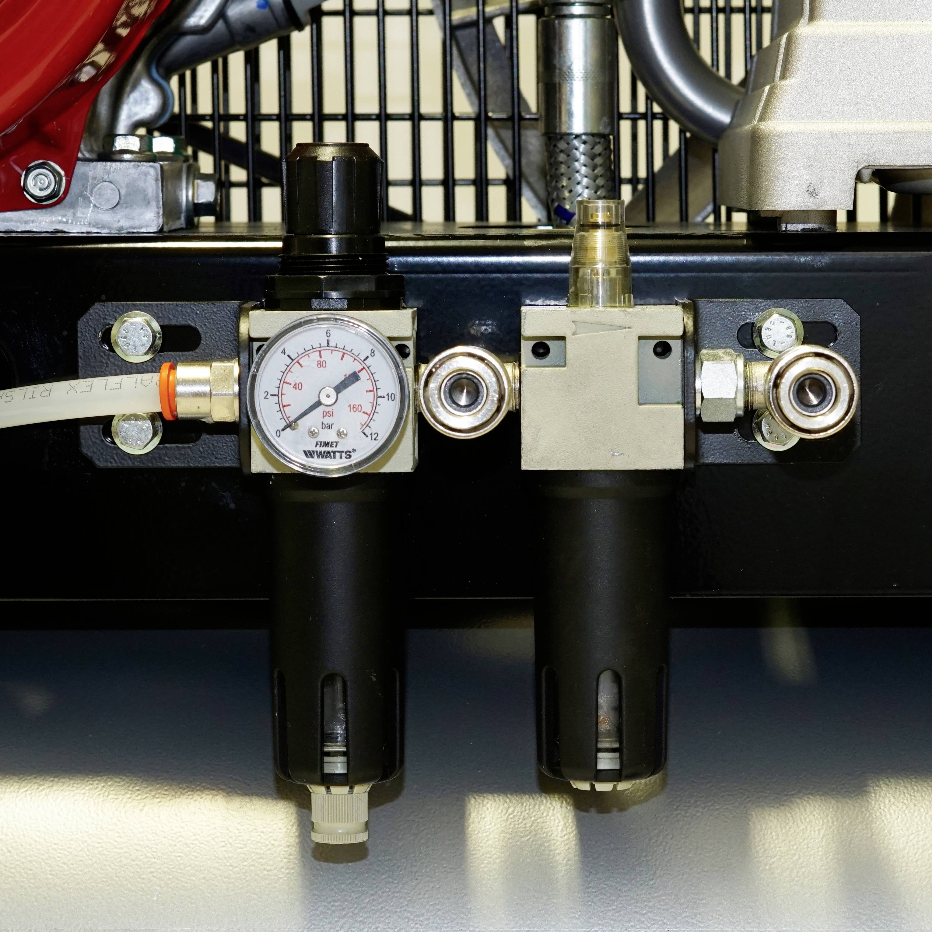 Regulator ciśnienia z manometrem i zaworem jest zamontowany na maszynie. Manometr wskazuje ciśnienie około 10 PSI.