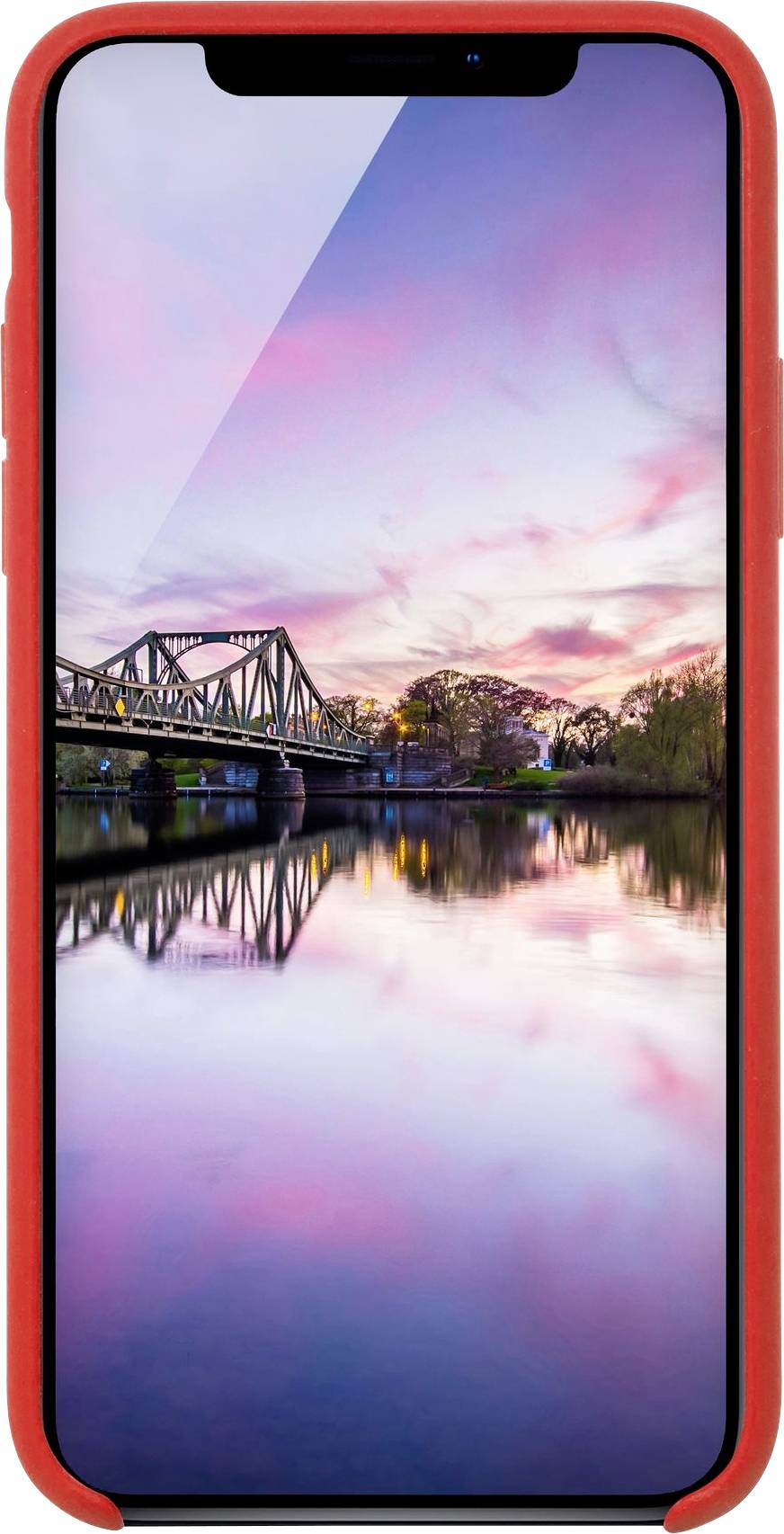 Smartfon w czerwonej obudowie wyświetla zdjęcie mostu o zachodzie słońca, a woda odbija kolorowe niebo.