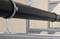 Czarne rury są zamocowane poziomo na metalowej konstrukcji za pomocą obejm mocujących. Otoczenie ma charakter przemysłowy.