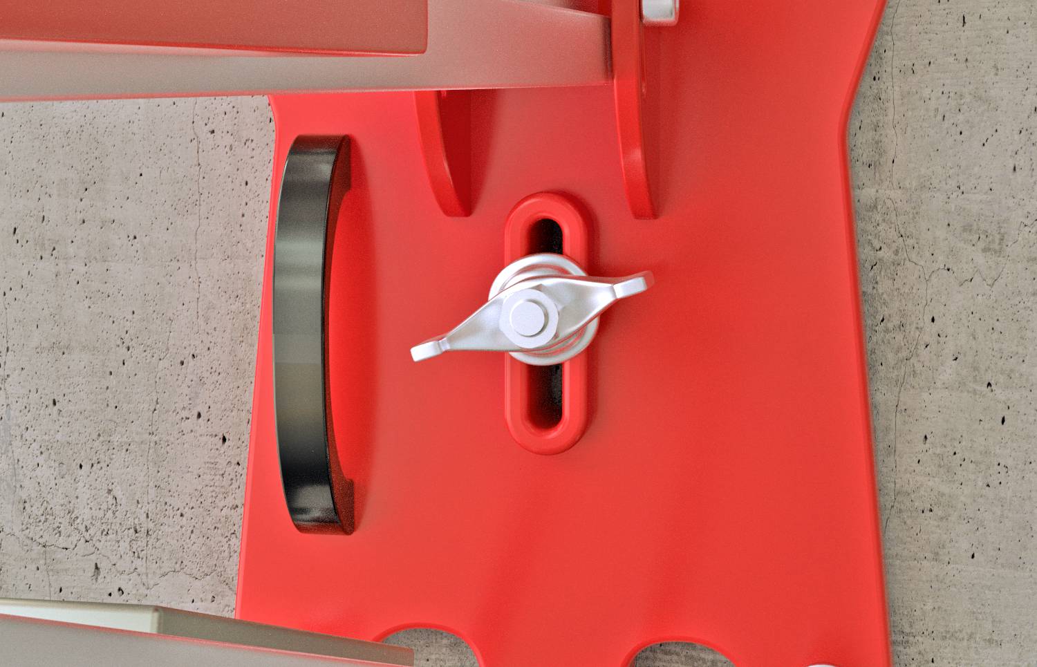 Czerwona część z tworzywa sztucznego z centralną, białą śrubą na tle szarej ściany betonowej. Po lewej stronie czarna rolka.