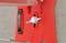 Czerwona część z tworzywa sztucznego z centralną, białą śrubą na tle szarej ściany betonowej. Po lewej stronie czarna rolka.