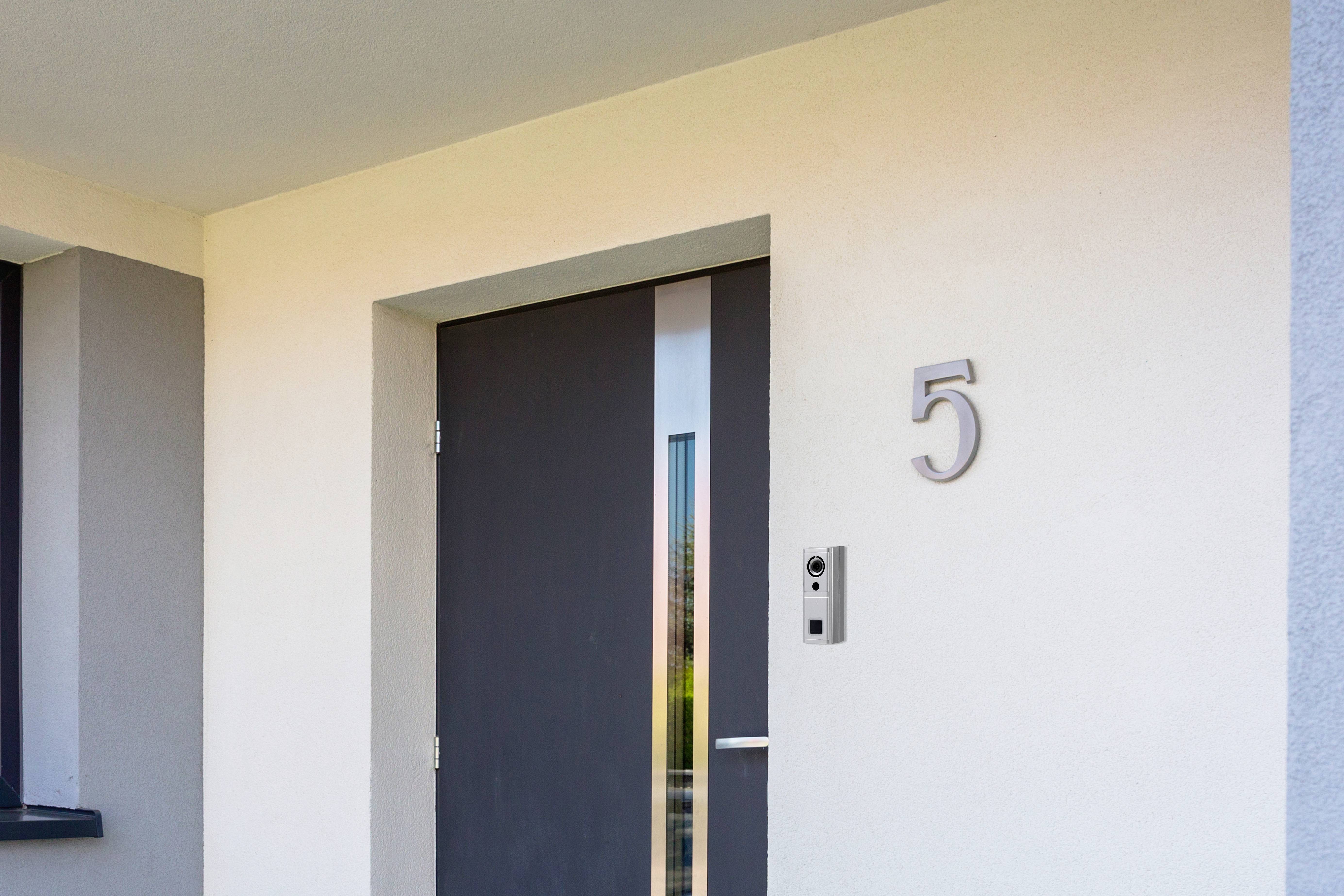Nowoczesne drzwi wejściowe przed jasnym budynkiem, z prawej strony numer domu '5' oraz dzwonek do drzwi z systemem domofonowym.