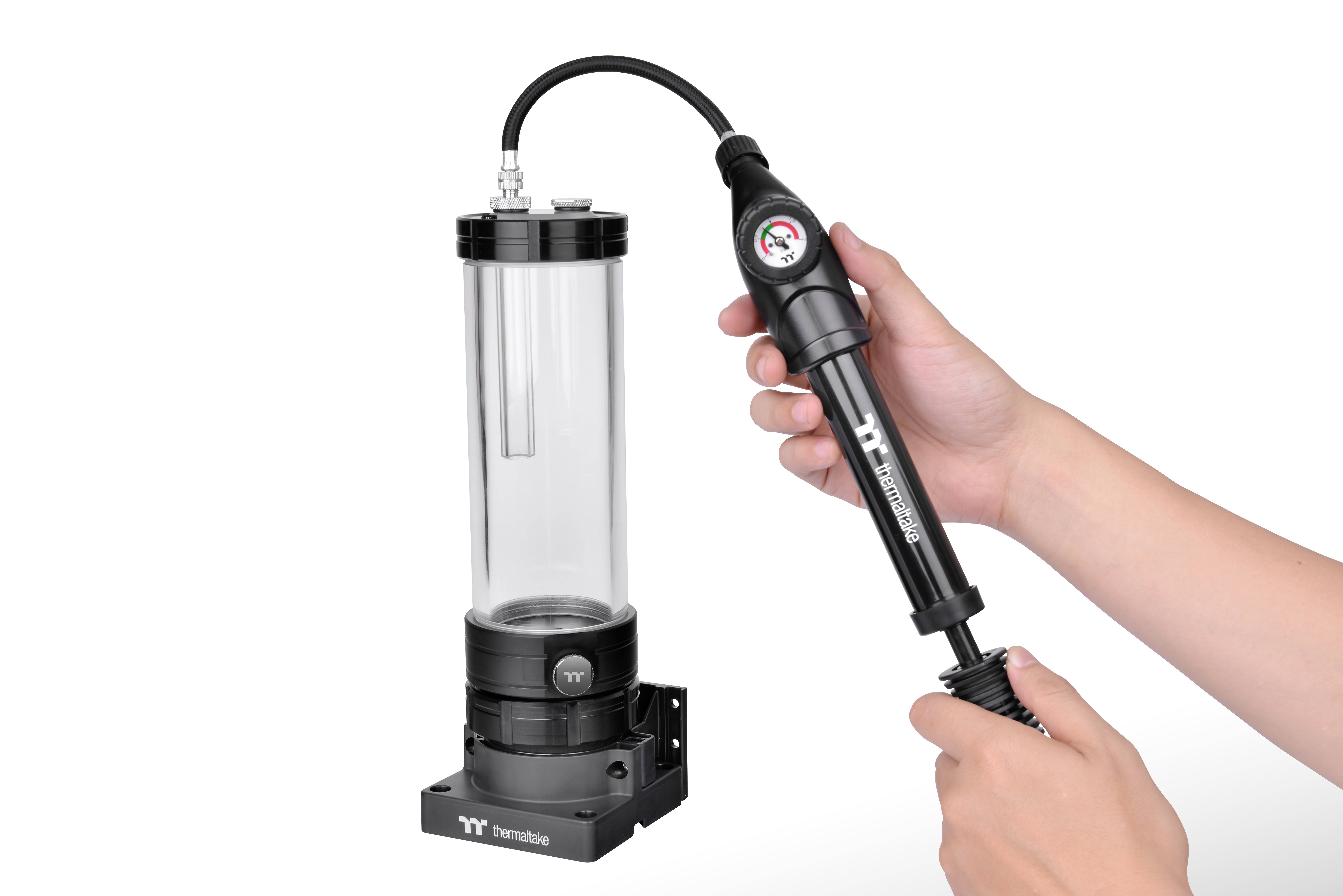 Ręka pompuje powietrze do przezroczystego zbiornika wodnego z czarną podstawą i manometrem, produkcji firmy Thermaltake.