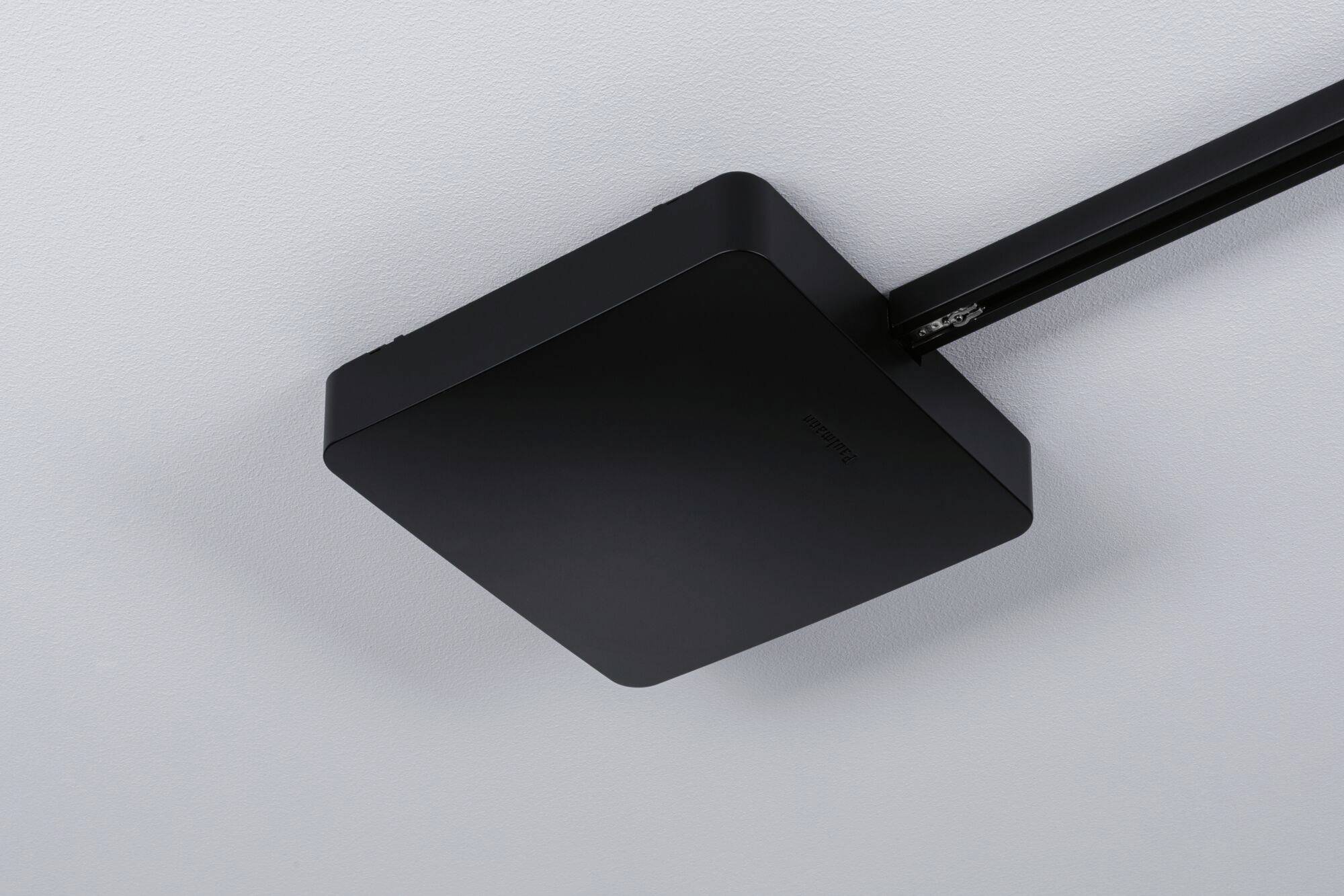 Czarny, kwadratowy obiekt sufitowy, prawdopodobnie urządzenie techniczne, zamontowany na czarnym słupie.