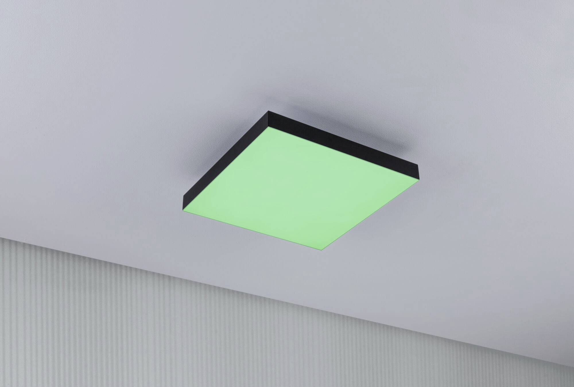 Prostokątna lampa sufitowa w pomieszczeniu, świecąca na zielono, zamontowana na białym suficie.