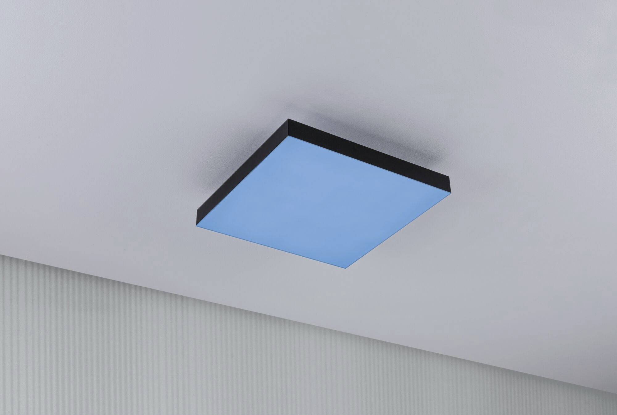 Kwadratowa, niebieska lampa sufitowa z czarną ramką zamontowana na białym suficie; nowoczesny i minimalistyczny design.