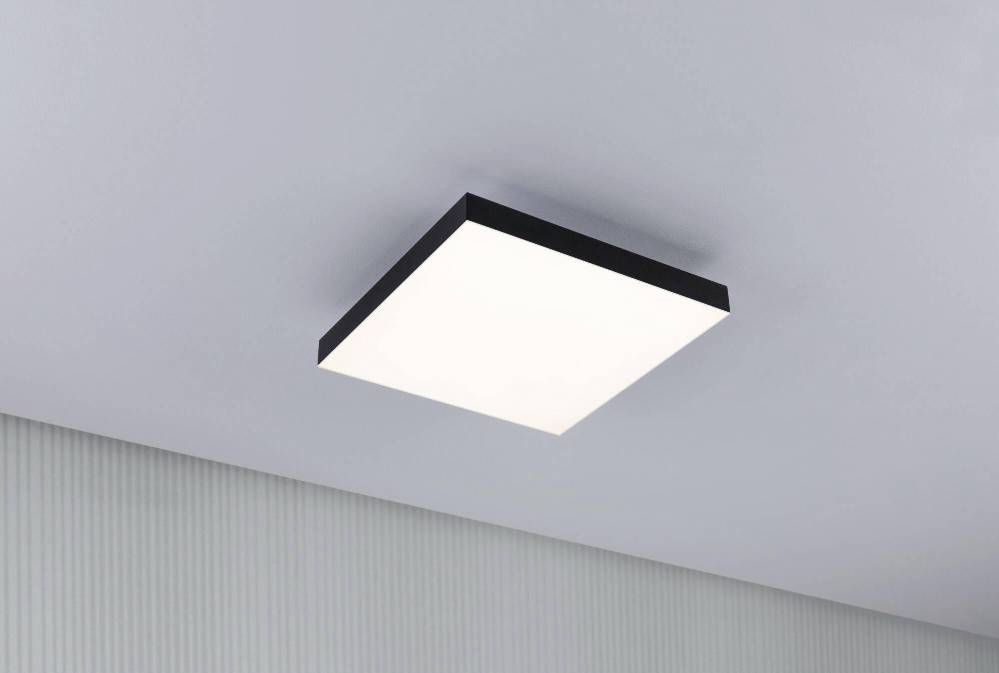 Prostokątna lampa sufitowa z czarną ramką, zamontowana na gładkim, szarym suficie. Świeci jasno i równomiernie.