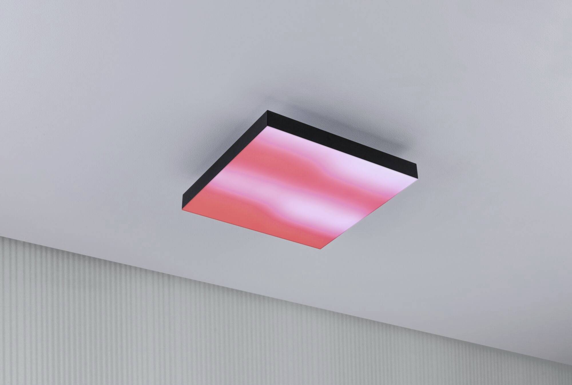 Prostokątna, czerwono świecąca lampa sufitowa na białym suficie, pomieszczenie o żebrowanej strukturze ścian.