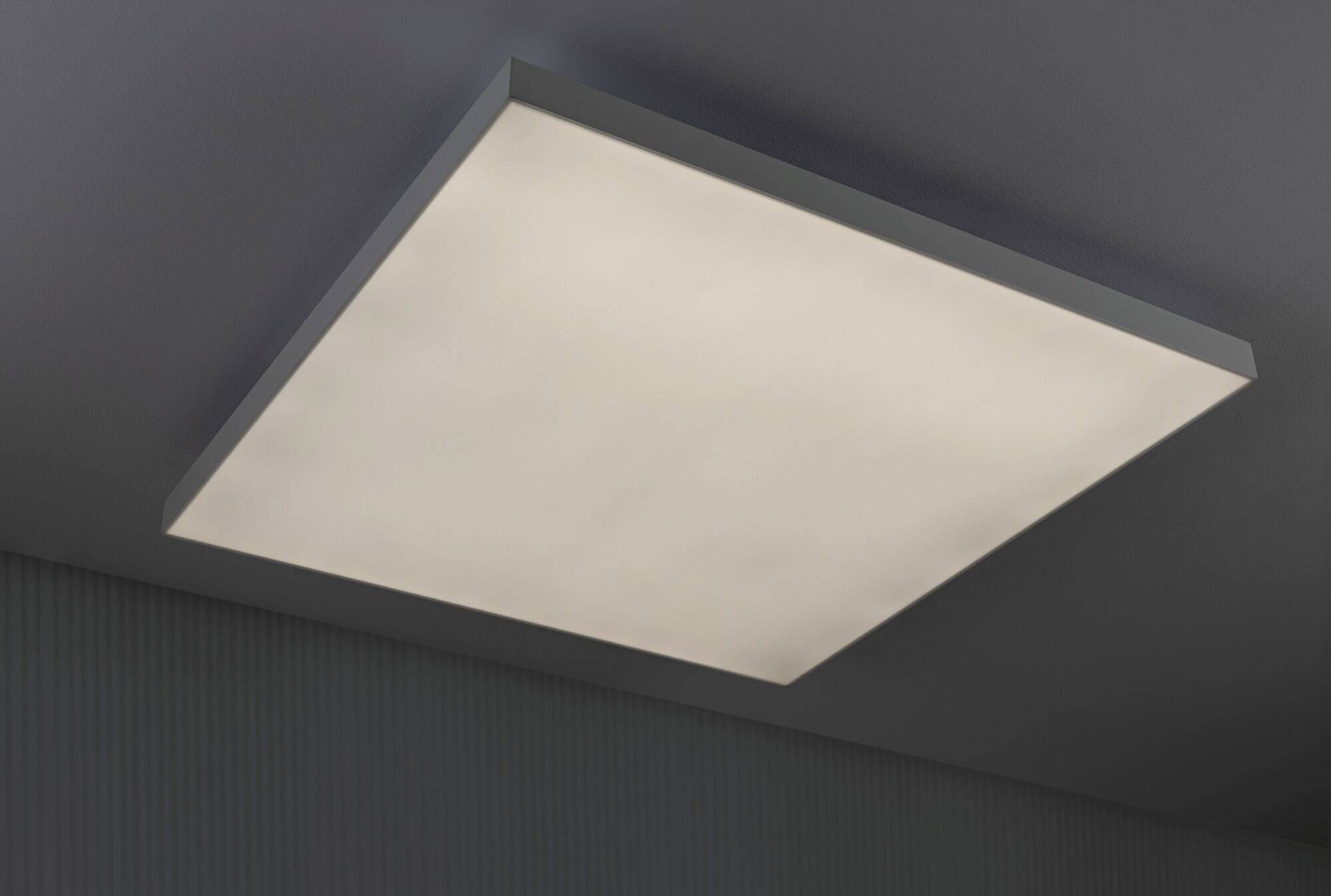 Prostokątne, płaskie światło sufitowe równomiernie oświetla pomieszczenie. Znajduje się na szarym suficie.