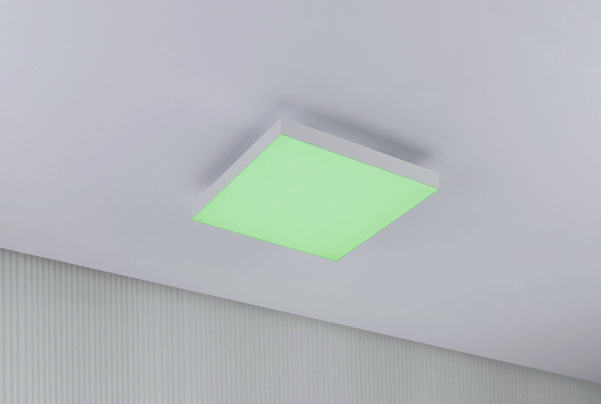 Prostokątna lampa sufitowa z zielonkawym światłem, zamontowana w nowoczesnym, jasnym pomieszczeniu.