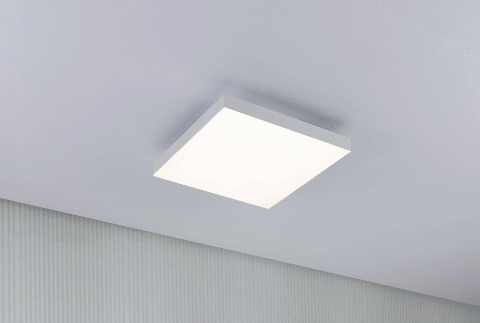 Prostokątna lampa sufitowa emituje równomierne, miękkie światło. Jest zamontowana na białym, strukturalnym suficie.