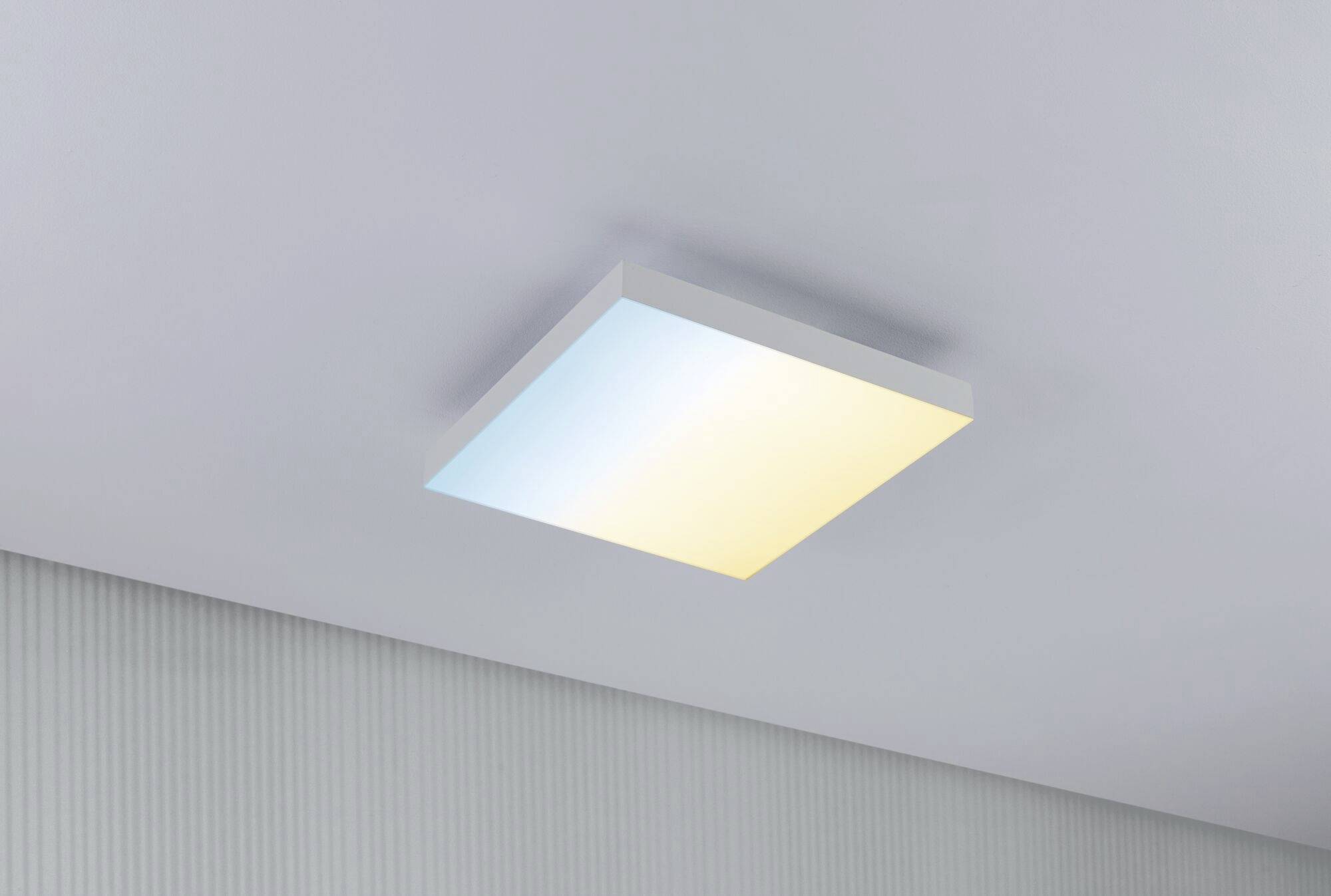 Kwadratowa lampa sufitowa z dwukolorowym światłem, niebieskim i żółtym, zamontowana w nowoczesnym pomieszczeniu.